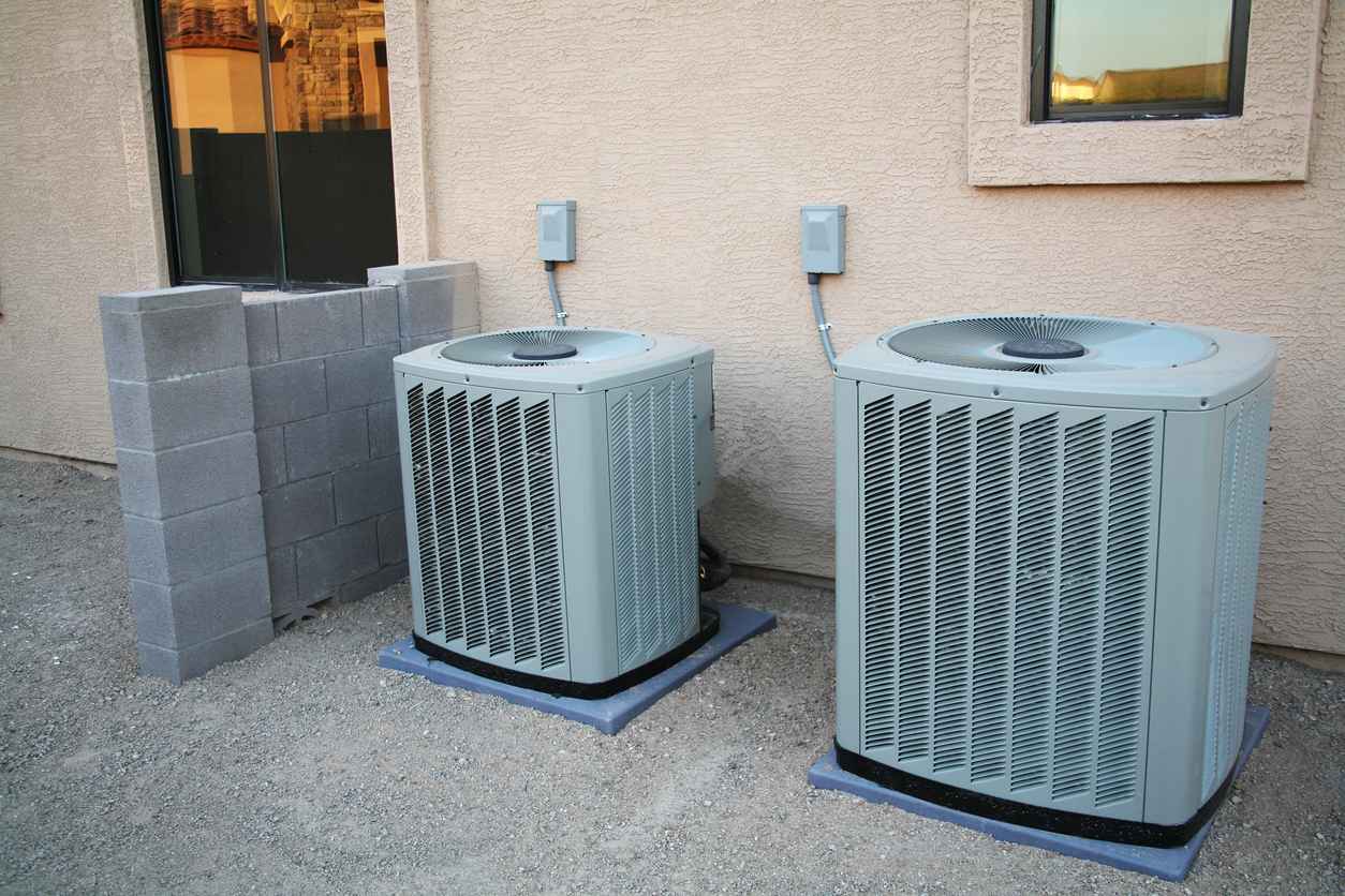 Two brand new central air conditioners sitting next to a new home.