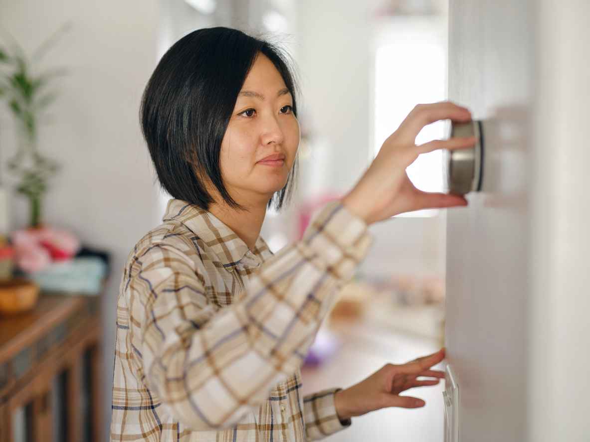 A woman in a home adjusting a smart thermostat